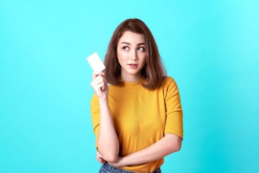 Young smiling beautiful woman in yellow shirt showing credit card in hand over blue background.