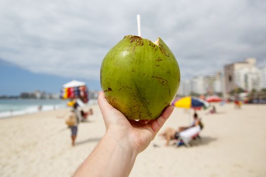 Fresh green coconut with a straw on a beach background