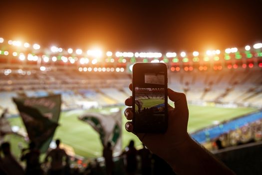 Smartphone photographing football game on the stadium.