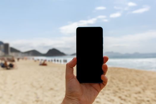 Using a smartphone on the beach. Blank black screen for your content