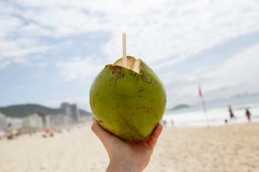 Fresh green coconut with a straw on a beach background