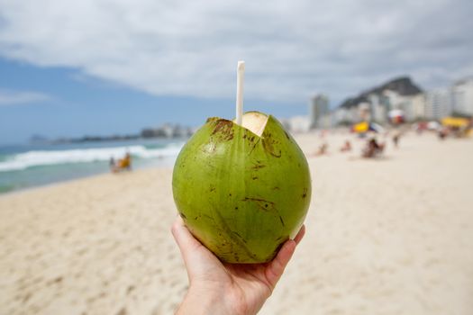 Fresh green coconut with a straw on a beach background