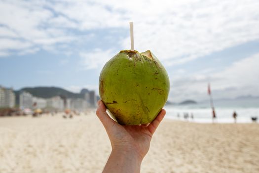 Fresh green coconut with a straw on a beach background