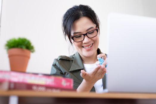 Modern young Asian woman cleaning hands with a gel cleanser before start working from home.