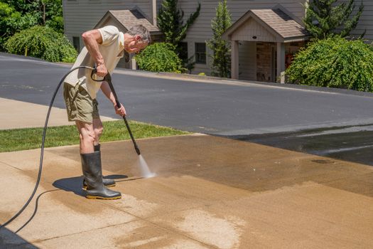 Senior caucasian man spraying concrete driveway with high pressure water spray to clean it