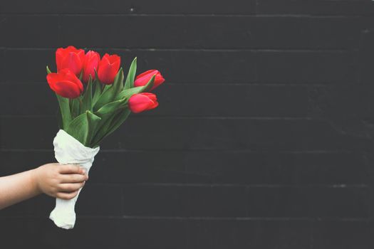 Little girl holding bouquet of red tulips against black brick wall; floral background