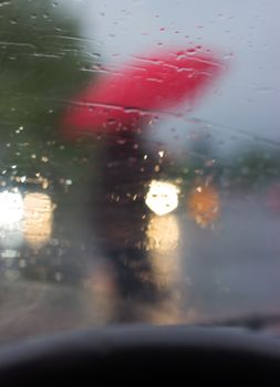 Behind the wheel - silhouette of a man with red umbrella, picture taken from the car, behind windshield