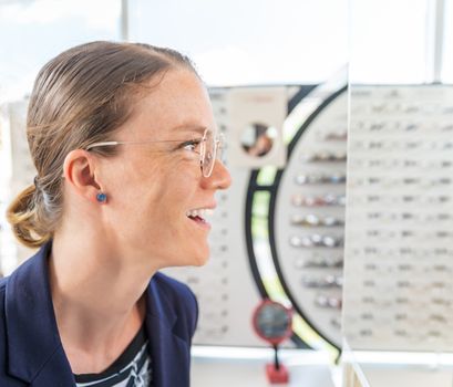 business woman tries glasses in front of a mirror in an optics store.