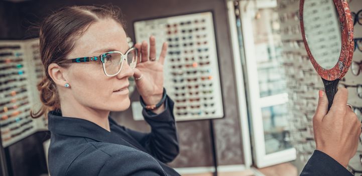 business woman tries glasses in front of a mirror in an optics store.