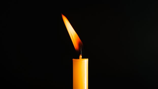 Close-up of a yellow candle illuminated in a black background.