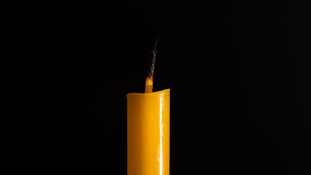 Close-up of a yellow candle illuminated in a black background.