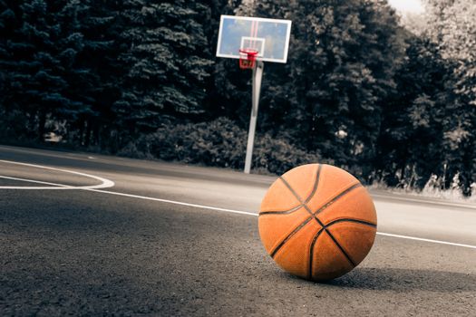 Basketball on the cover of a sports field against the background of a basketball ring and trees in gray tones