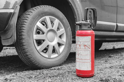 A fire extinguisher stands on the ground near the car as fire safety