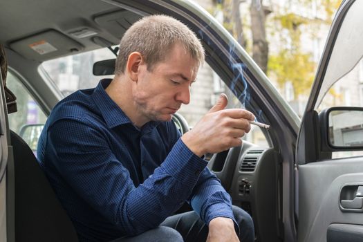 The detained intruder sits in handcuffs in his car and smokes a cigarette