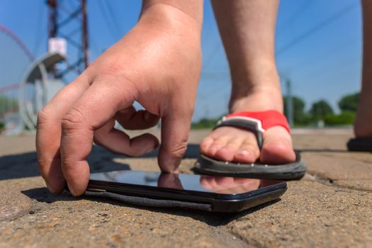 A man picks up a mobile phone that fell on the road in a public park in the summer