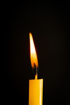 Close-up of a yellow candle illuminated in a black background.