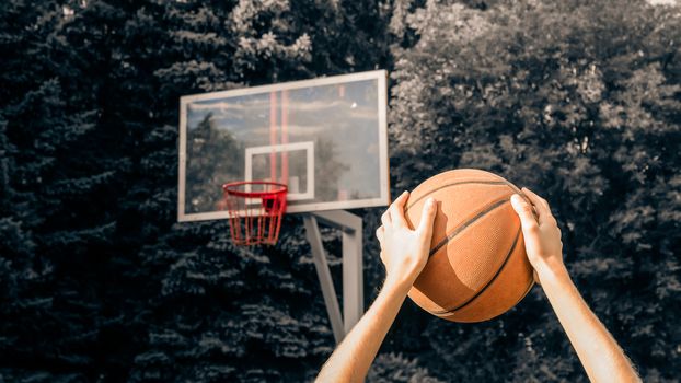 Hands of a teenager holding a basketball over his head before throwing into the basket during a match in street basketball