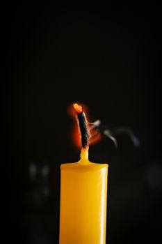 Close-up of yellow candles that are extinguished and smoke in a black background.