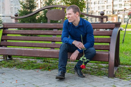 Displeased man with a rose in his hands is watching someone in the park