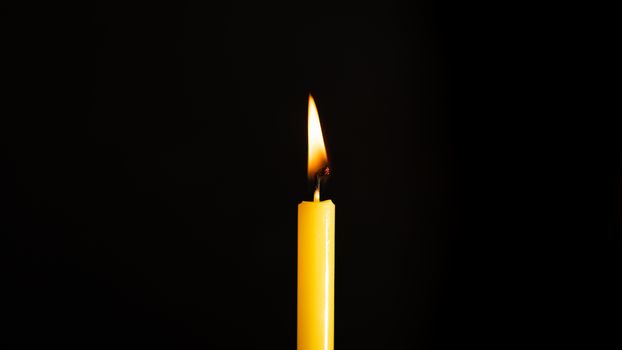 Close-up of a yellow candle illuminated in a black background.