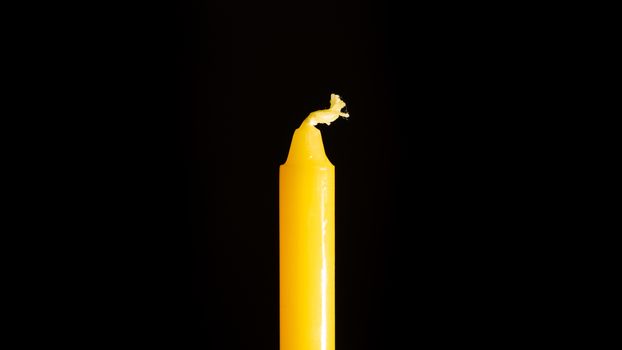 A close up of a yellow candle in a black background