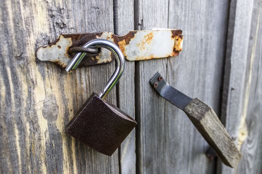 An open padlock hanging on the wooden doors of an old barn