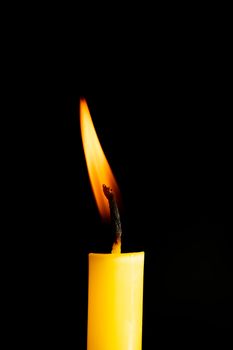 Close-up of a yellow candle illuminated in a black background.