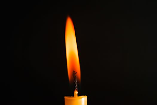 Close-up of a yellow candle illuminated in a black background.