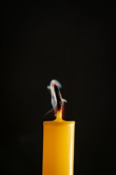 Close-up of yellow candles that are extinguished and smoke in a black background.