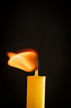 Close-up of a yellow candle illuminated in a black background.