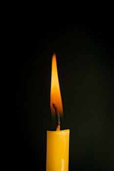 Close-up of a yellow candle illuminated in a black background.