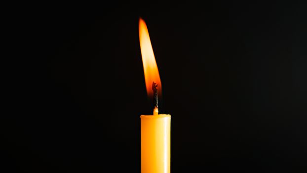 Close-up of a yellow candle illuminated in a black background.