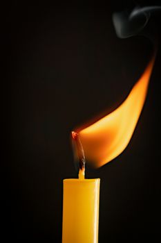 Close-up of a yellow candle illuminated in a black background.