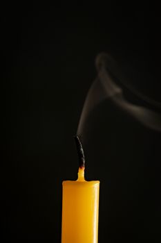 Close-up of yellow candles that are extinguished and smoke in a black background.