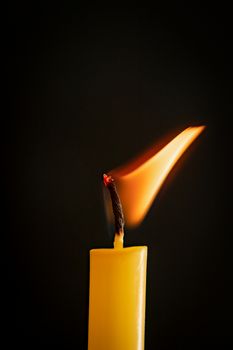 Close-up of a yellow candle illuminated in a black background.