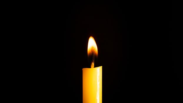 Close-up of a yellow candle illuminated in a black background.