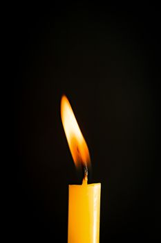 Close-up of a yellow candle illuminated in a black background.