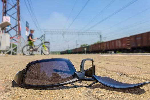 The broken glasses lie at the railway station against the background of passing by the boy by bicycle and moving train