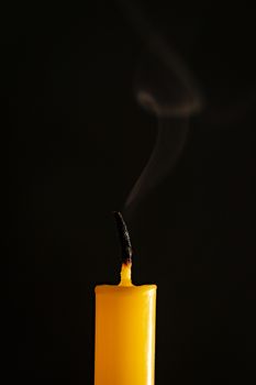 Close-up of yellow candles that are extinguished and smoke in a black background.