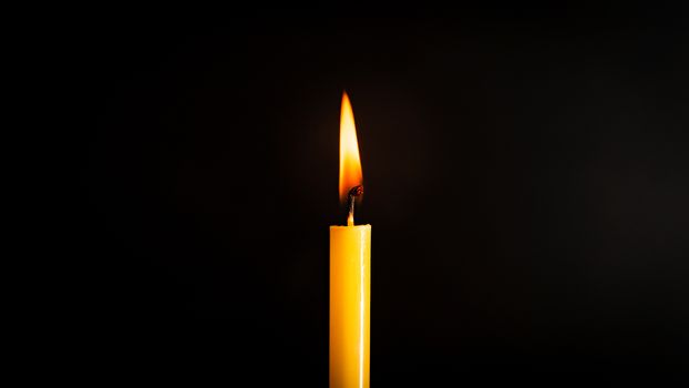 Close-up of a yellow candle illuminated in a black background.