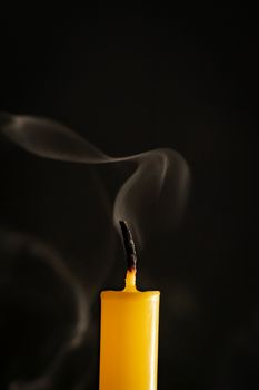 Close-up of yellow candles that are extinguished and smoke in a black background.