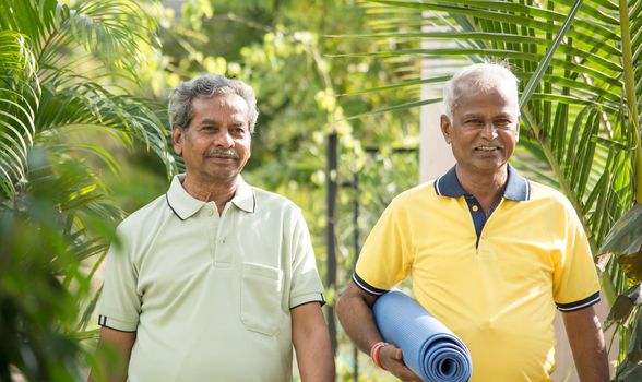 Happy Senior people with yoga mat in park - Healthy elderly men with fitness mat outdoor - older joyful friends walking in garden during morning.