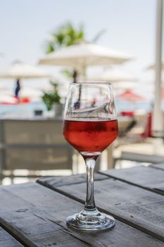 Summer wine day view of half-full glass of alcoholic drink on a wooden table with blurred beach restaurant view background and copy space.