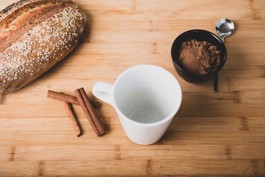 Top view of flat lay on wooden table of black cup with cocoa, bread and cinnamon