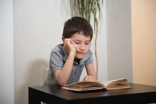 Schoolboy with a bored face flips through a book