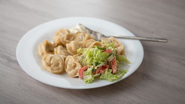 dumplings with vegetable salad on a white plate and a light wooden table
