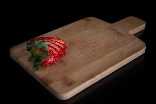 sliced strawberry rests on a wooden board with a place for text and a black background