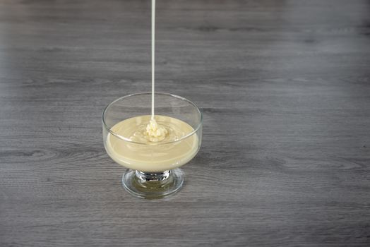 condensed milk in a transparent glass bowl on a gray wooden background