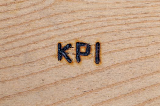 an abbreviation KPI - key performance indicator - burned by hand with electric wood burner on plywood surface.