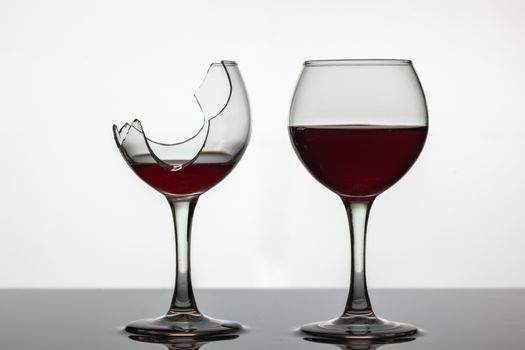Broken and not broken wine glass with red wine on white background.